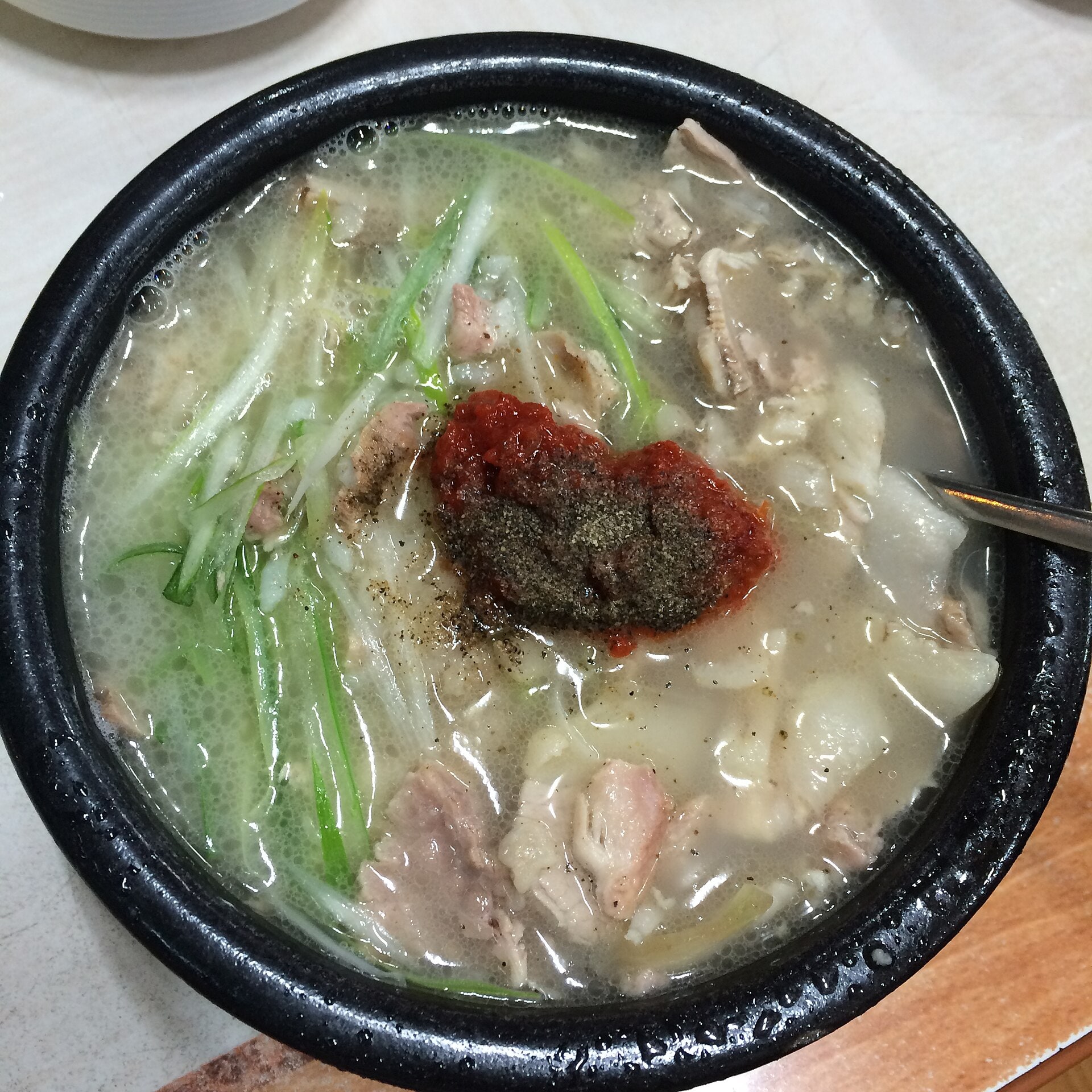 고기와 파가 담긴 돼지국밥 가운데 붉은 다대기를 올린 모습
