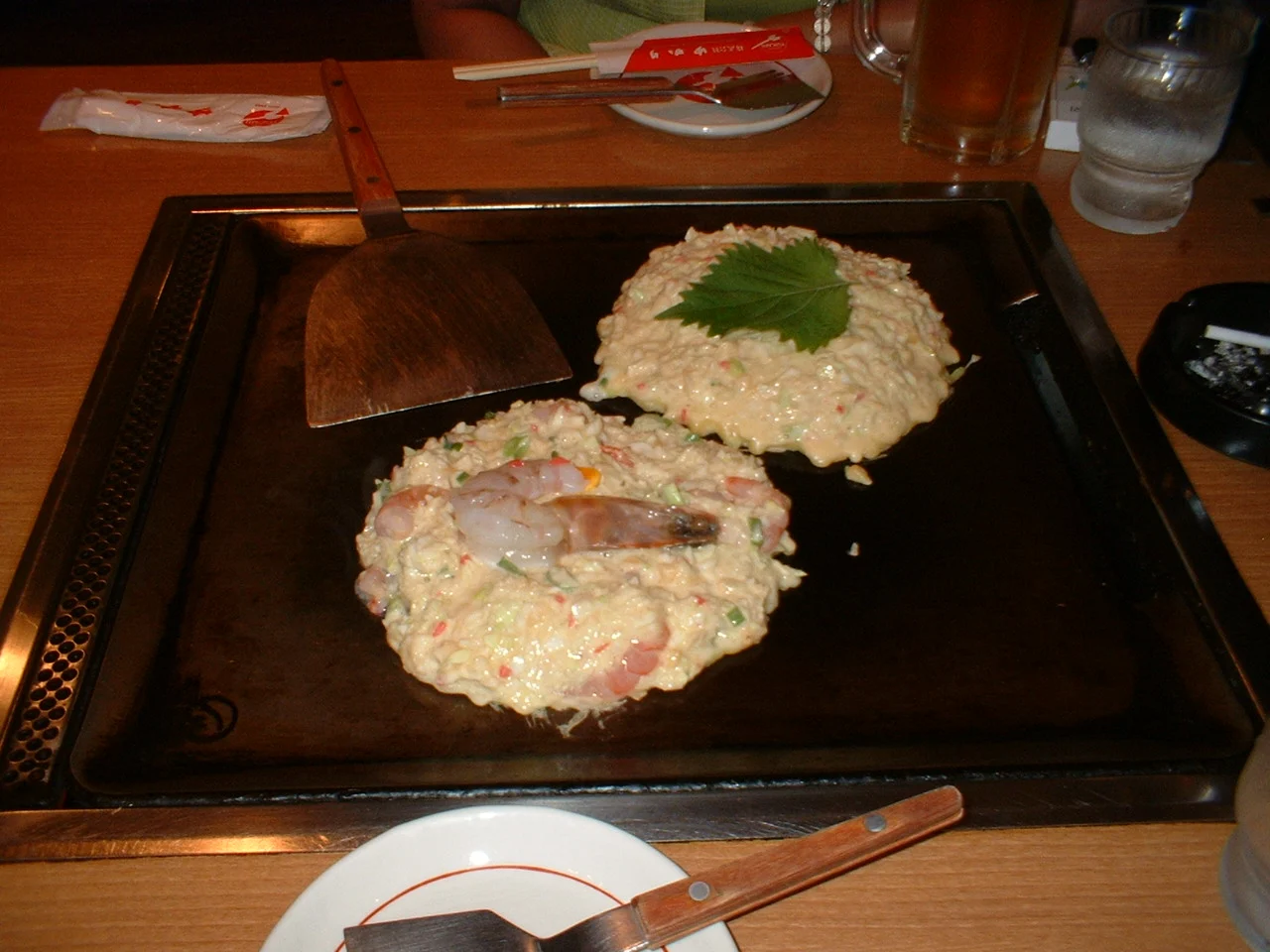 오사카 덴포잔 식당 철판 위 재료가 섞인 두 장의 반죽, 앞쪽 새우와 넓은 금속 헤라