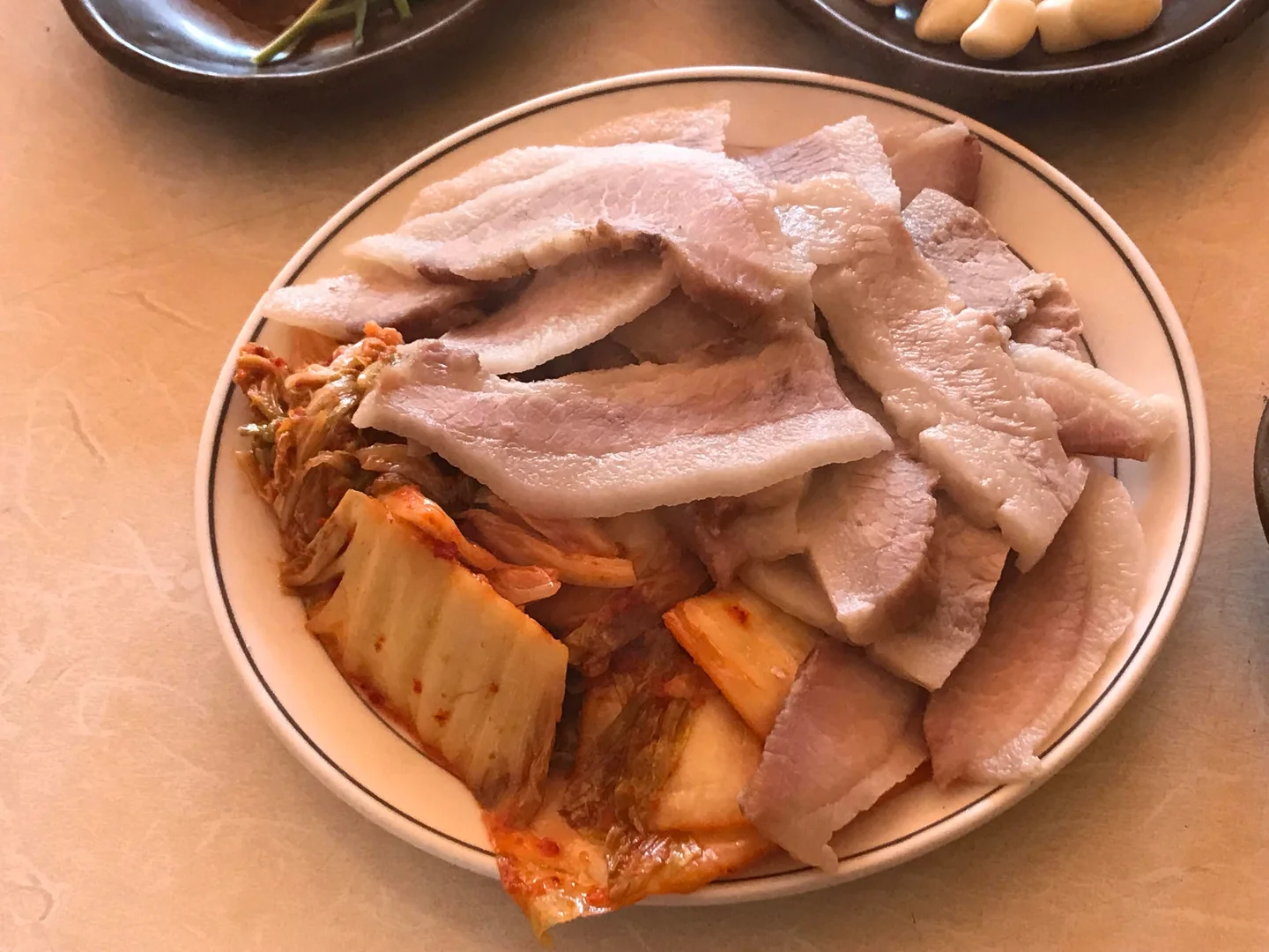 김치를 곁들인 접시에 삶아 썬 돼지고기가 여러 겹 놓인 모습