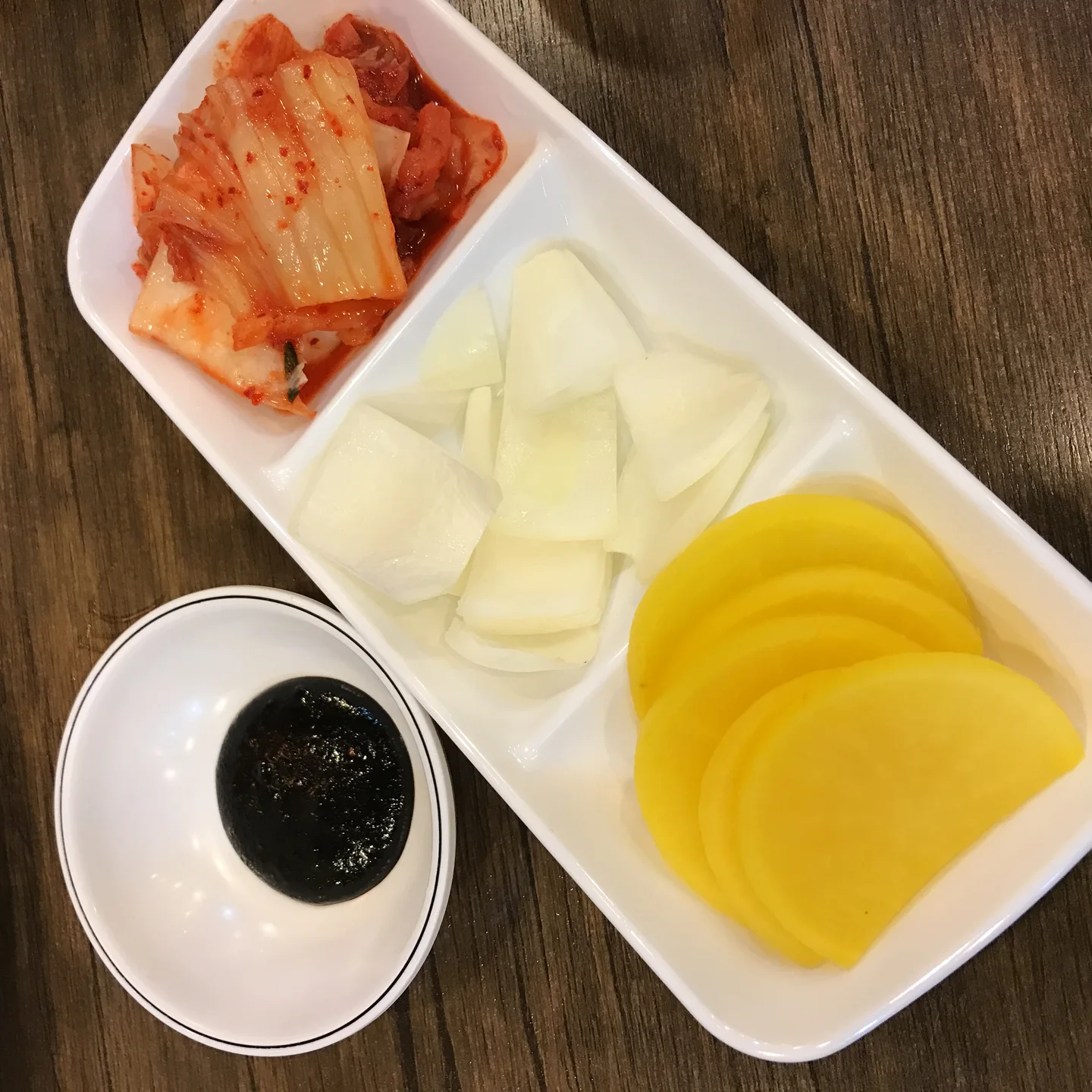 작은 그릇에 담긴 검은 춘장과 칸을 나눠 담은 생양파, 노란 단무지, 김치