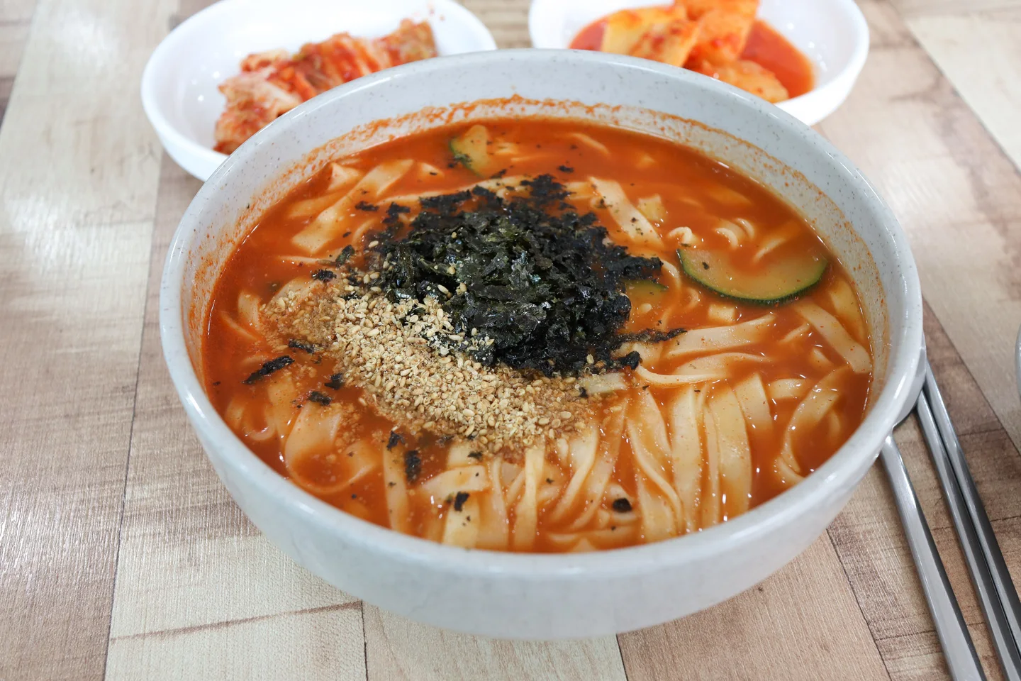 붉은 국물과 넓은 면 위에 검은색과 갈색 고명을 얹은 장칼국수