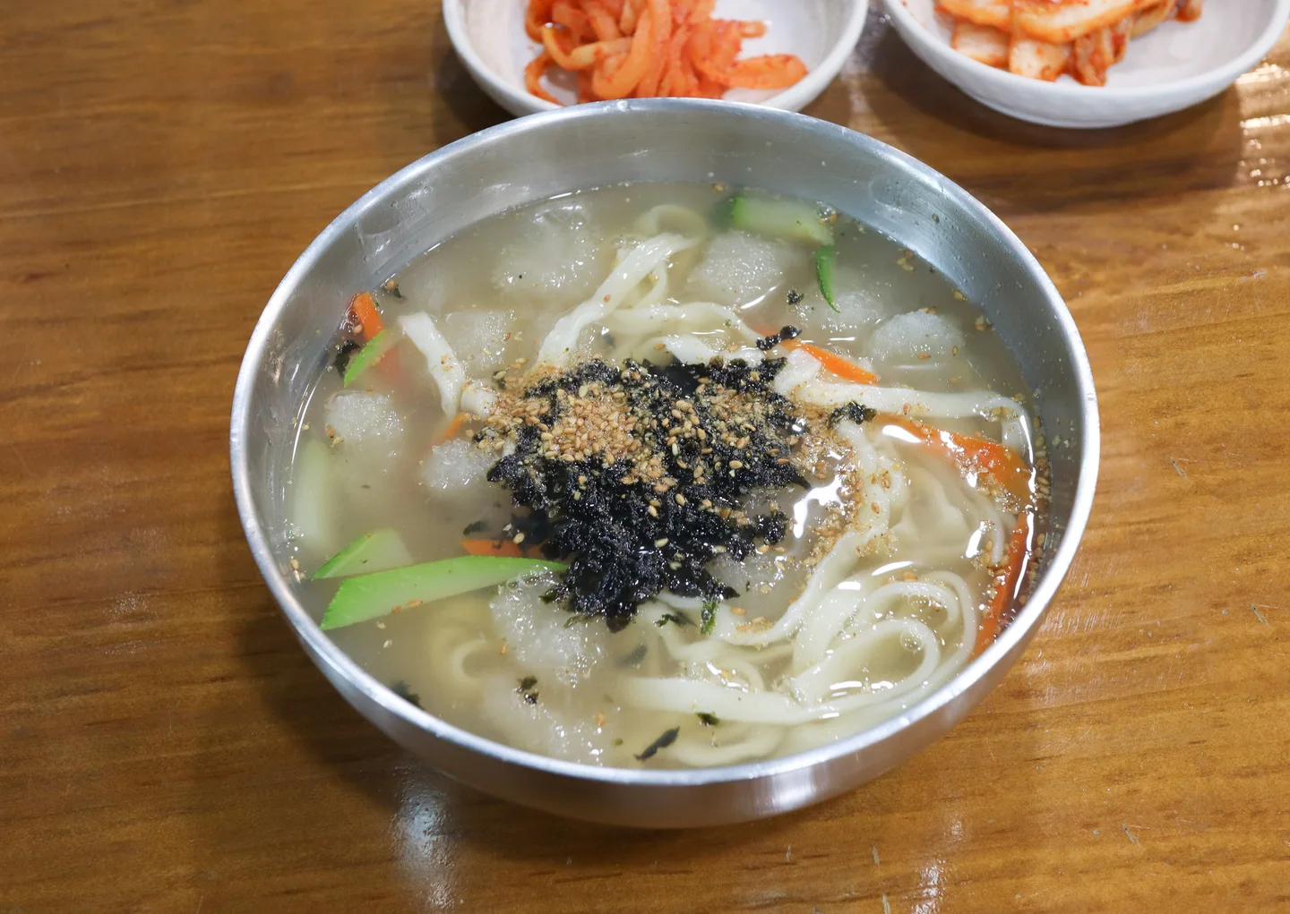 긴 칼국수 면과 둥근 감자옹심이가 함께 담긴 금속 그릇