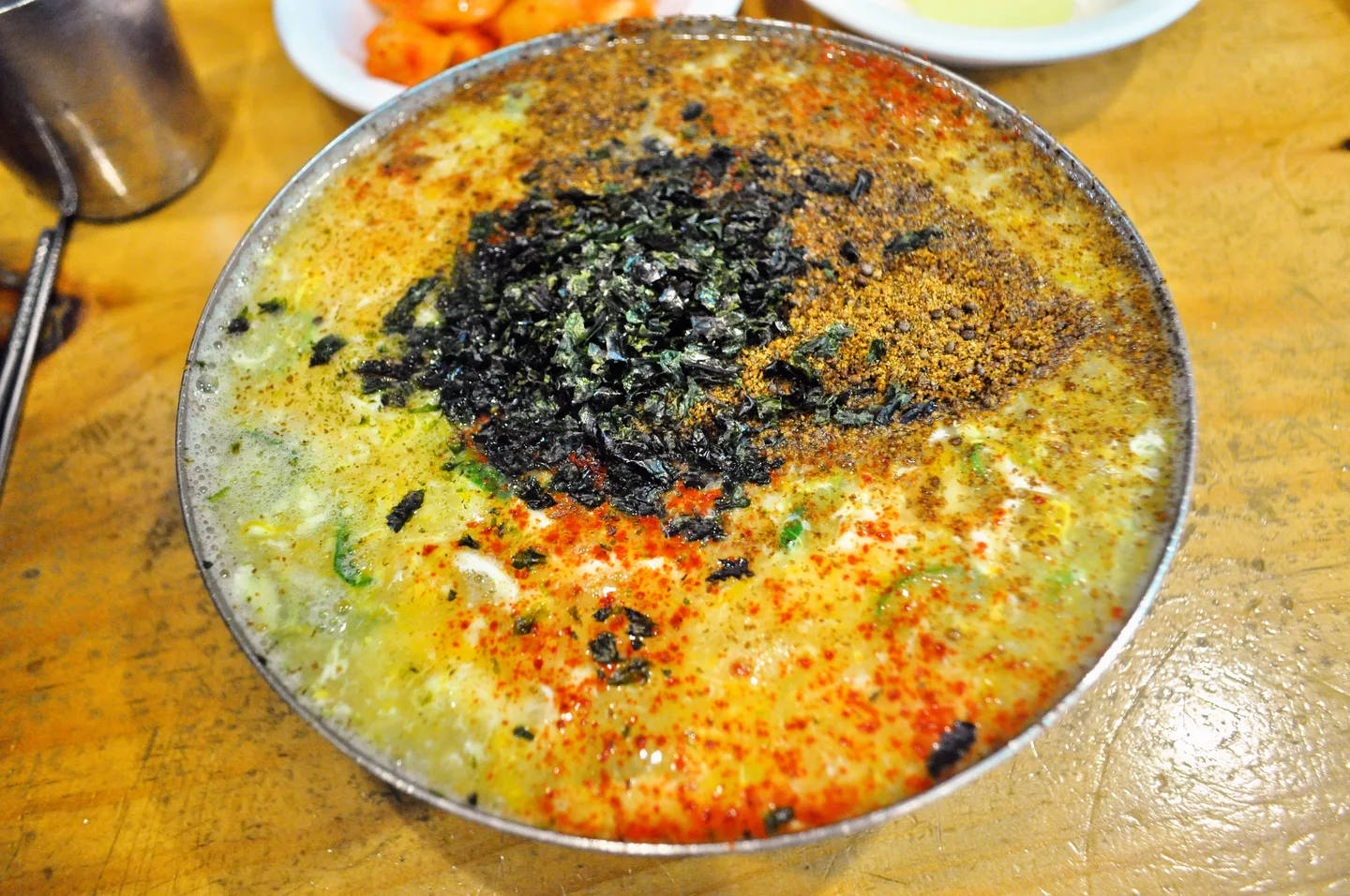 국물 표면에 들깨가루와 검은 고명, 붉은 양념이 넓게 올라간 칼국수 한 그릇