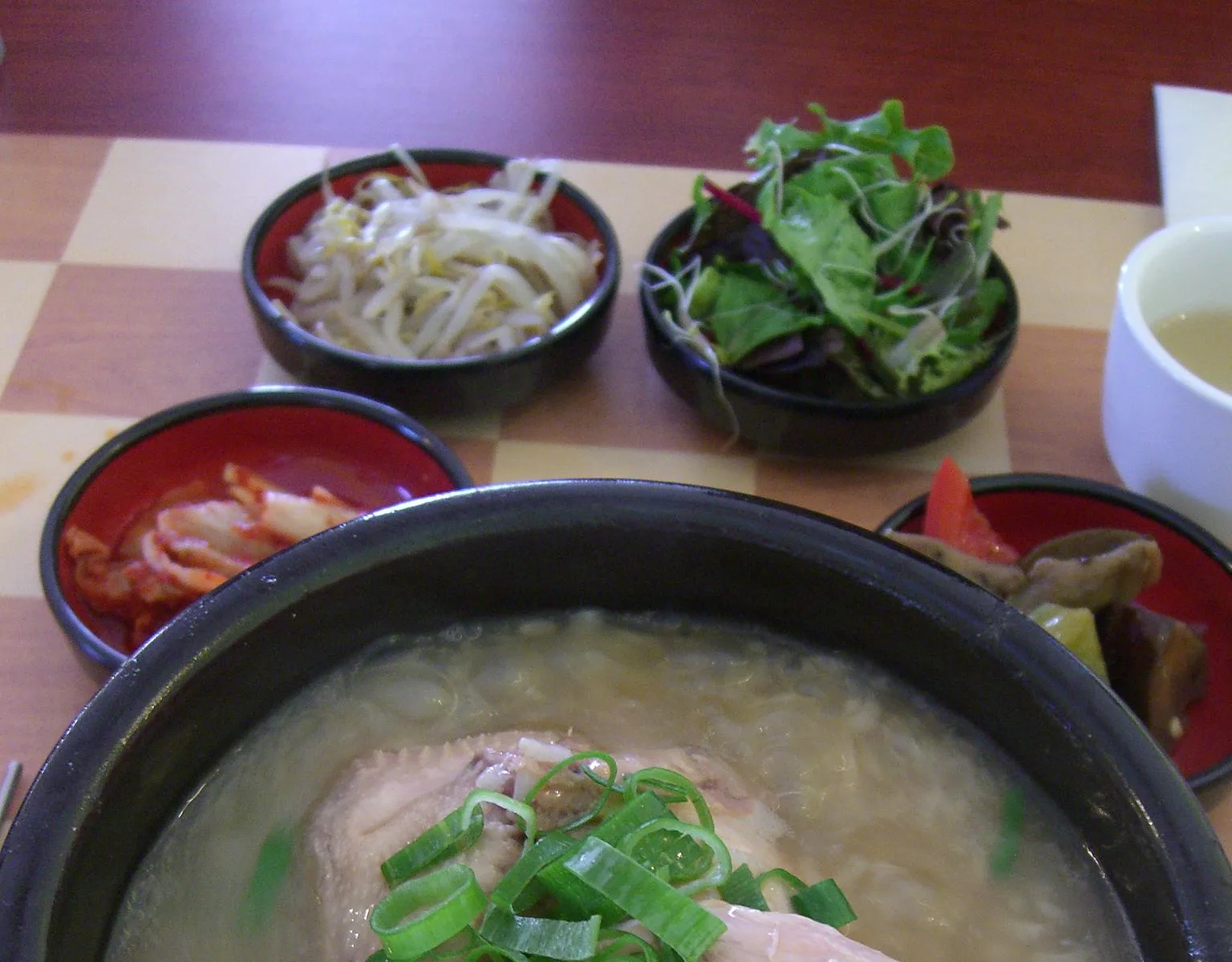 닭 한 마리와 파를 담고 반찬을 곁들인 삼계탕 상