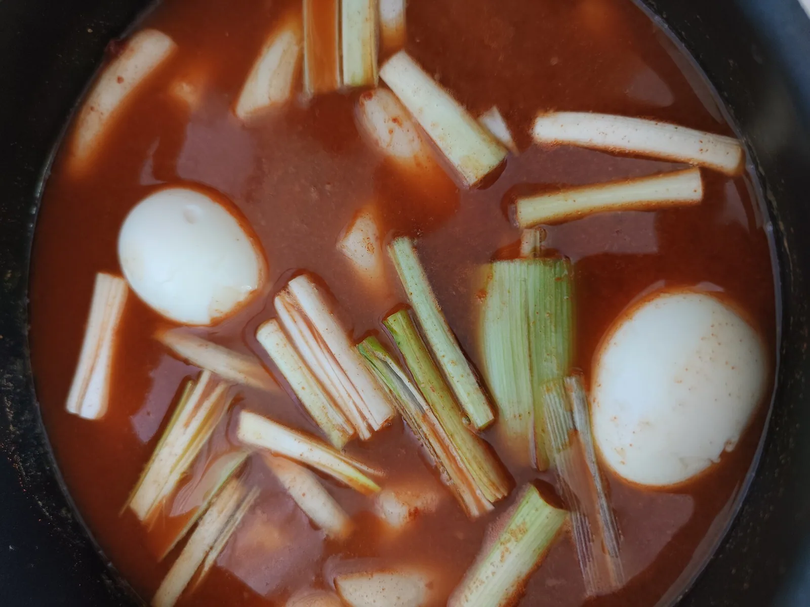 붉은 국물에 떡과 길게 썬 파, 삶은 달걀 두 개가 잠긴 냄비