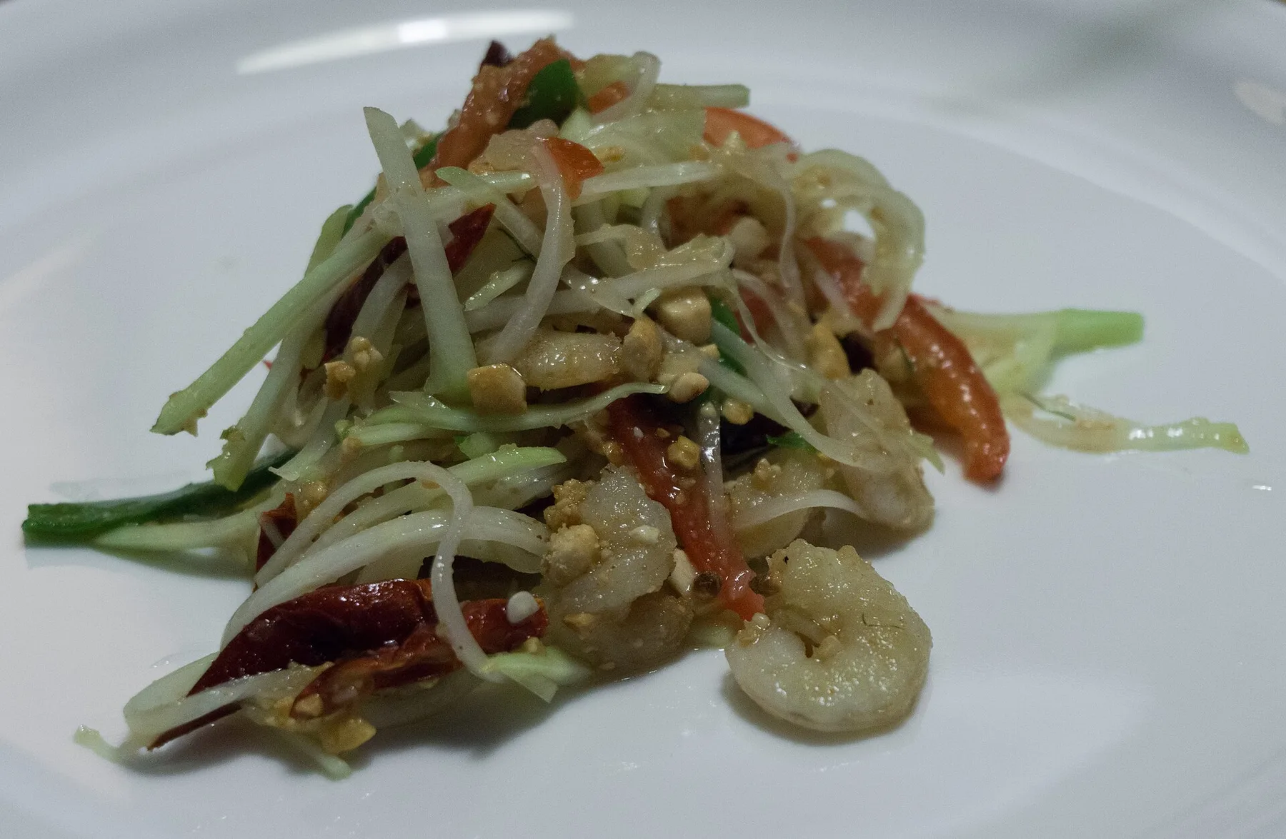흰 접시에 풋파파야와 토마토, 마른 새우를 담은 솜땀