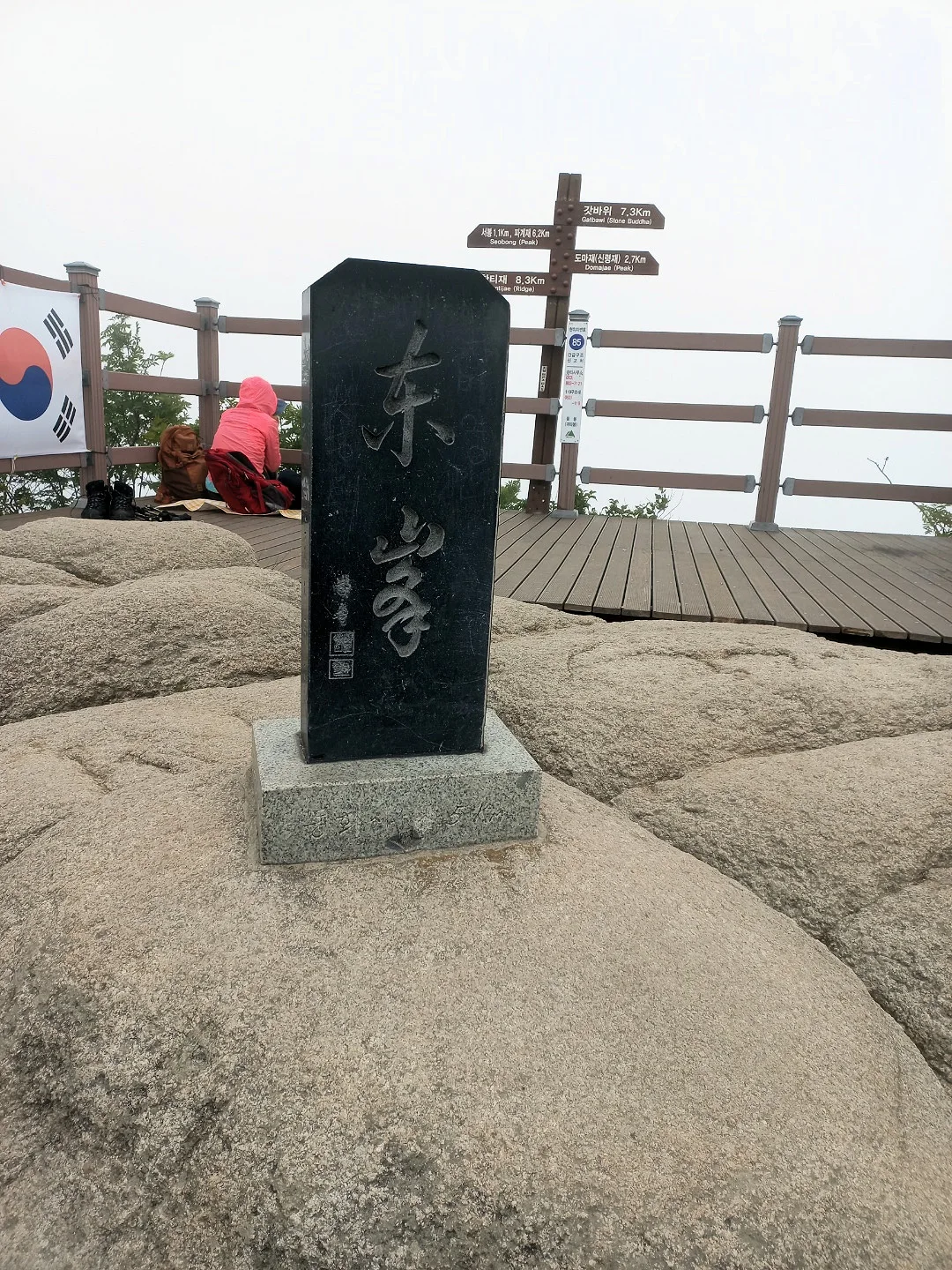 바위 위의 팔공산 동봉 표지석과 뒤쪽 목재 데크